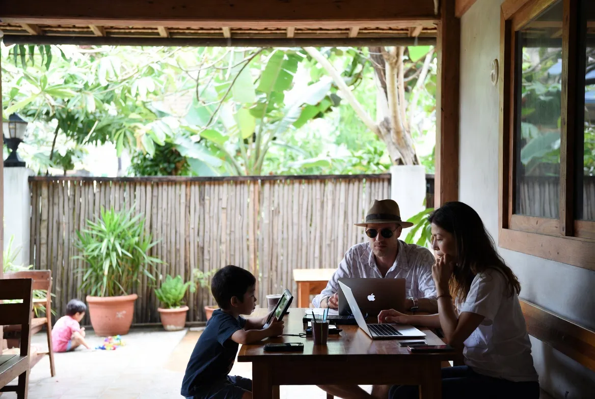 Digital nomad parents working in a cafe while kids play nearby in Bali